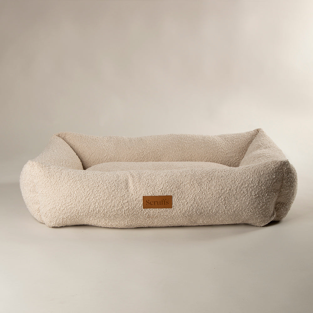 Beige dog bed with a brand logo on a light grey background