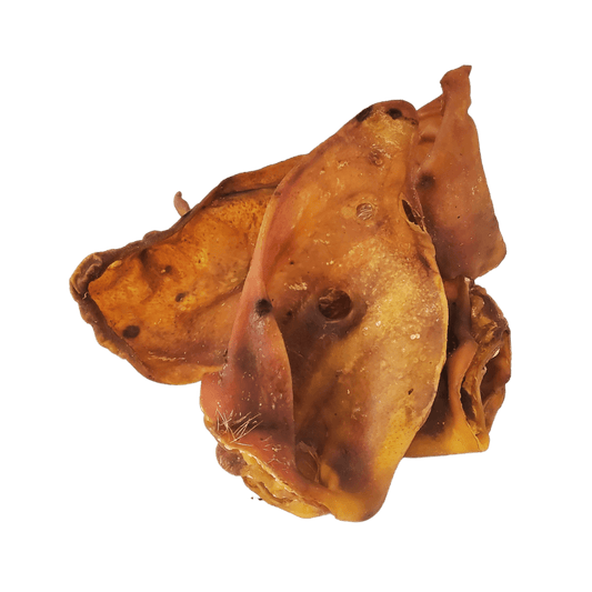 Three pigs ears natural dog treats stacked on top of each other on an all white background.
